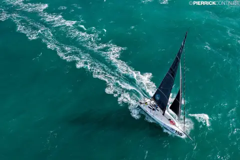 Le Class40 vu du ciel, avec son sillage blanc sur une mer turquoise