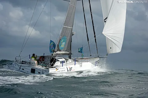 Le Class40 sous voile d'avant blanche, sous un ciel nuageux