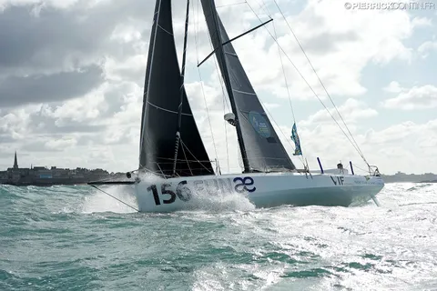 Le Class40 sous voiles noires, une côte à l'arrière-plan