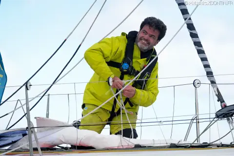 Loïc Féquet souriant, une main sur des cordages, sur le pont de son Class40